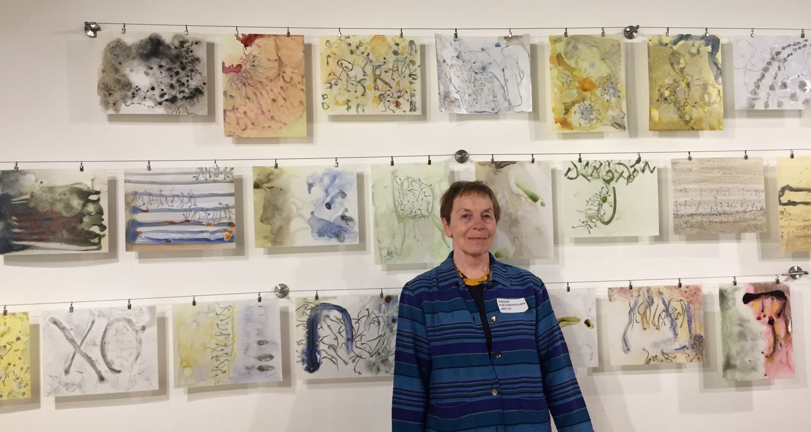 Image of artist in front of a wall of yupo artworks hung on three lines.